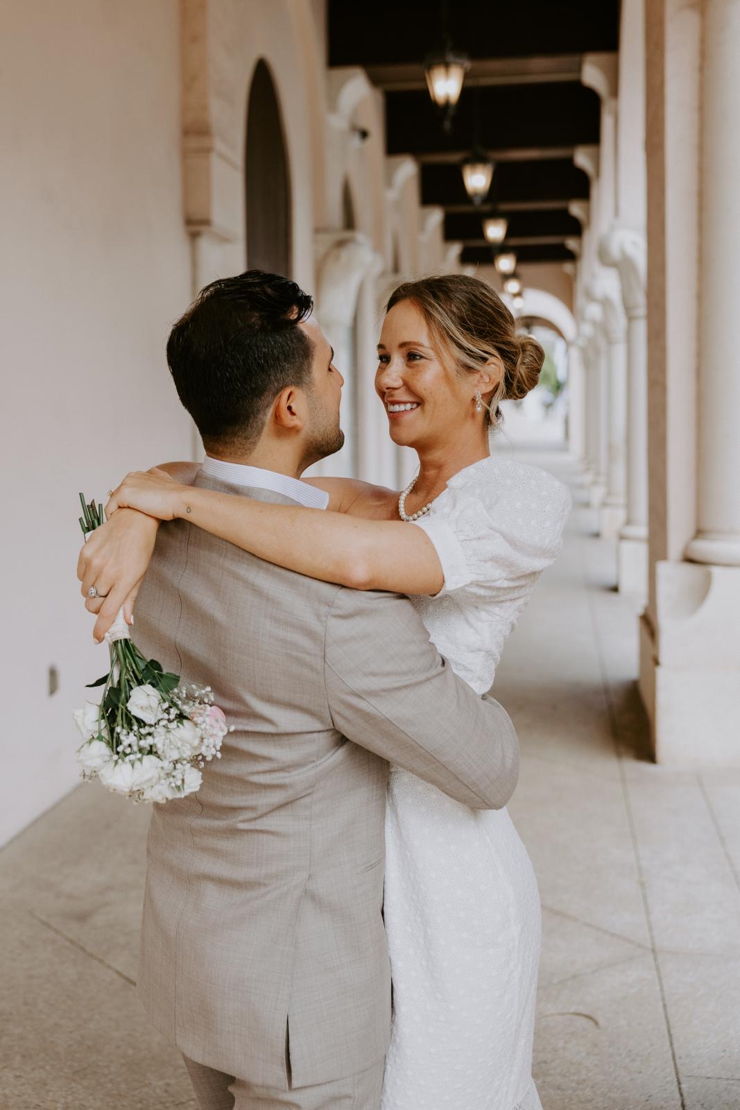 Bride and groom embracing beneath historic courtyard arches in Boca Raton