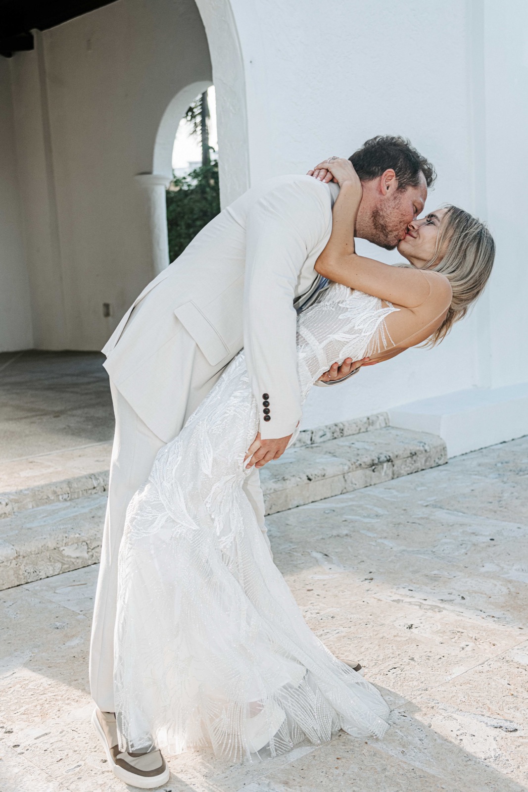 Groom dipping the bride for a kiss beneath a white archway in Palm Beach
