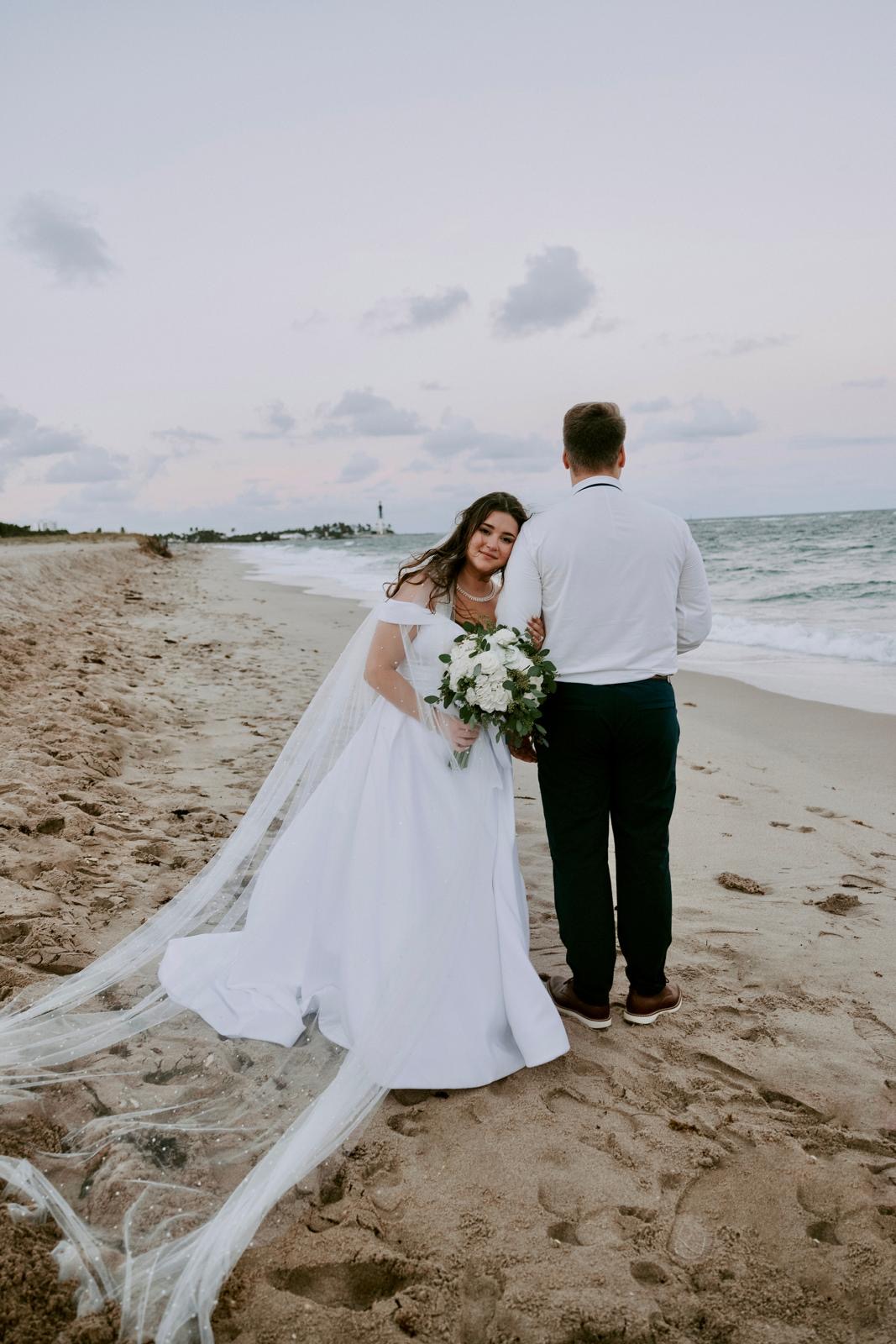 Bride resting on the groom's arm on the sand near Hillsboro Lighthouse