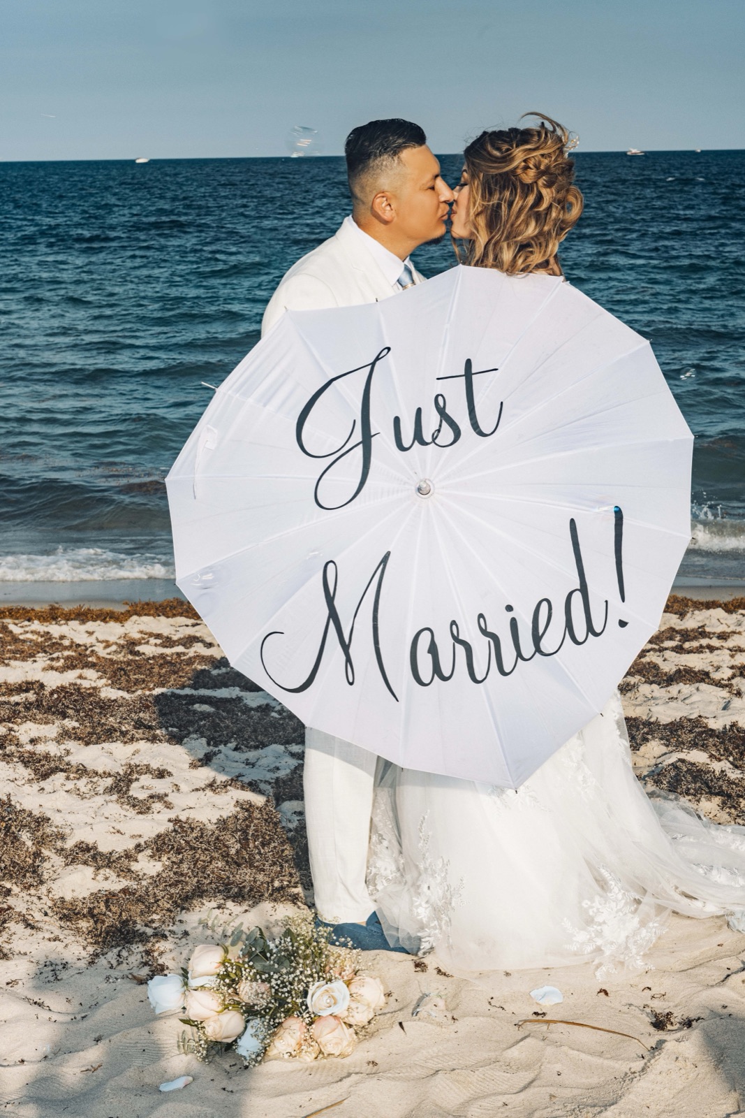 Newlyweds kissing behind a Just Married umbrella on a South Florida beach