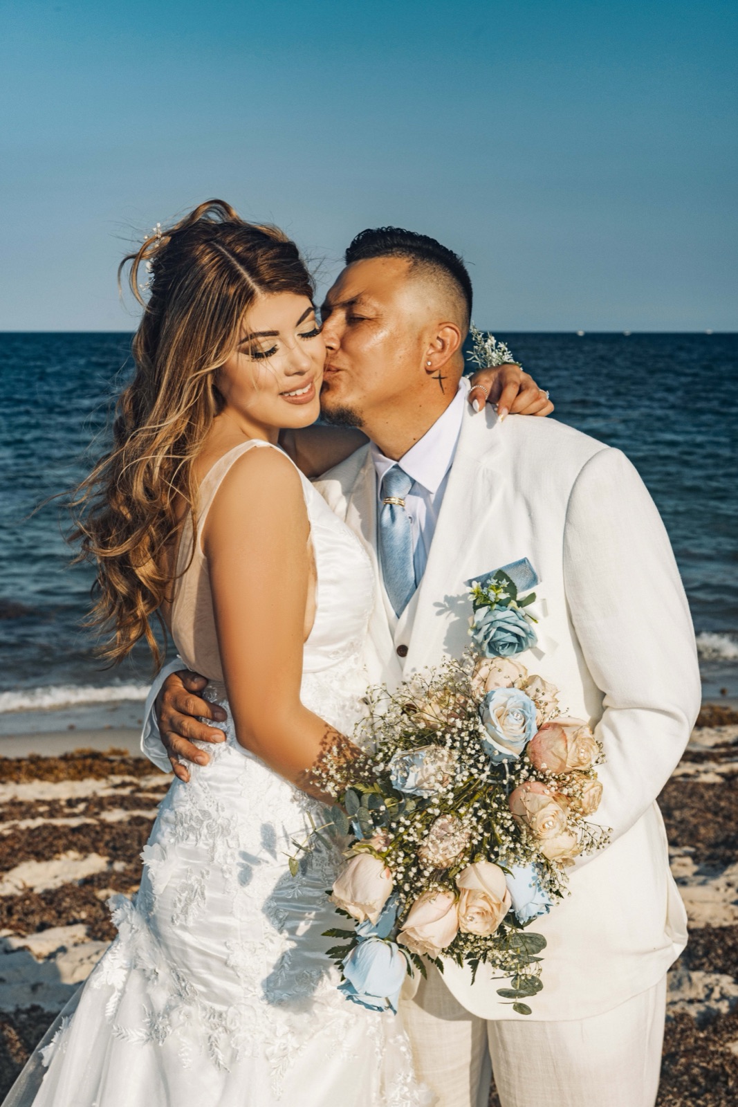 Groom kissing the bride's cheek, pastel bouquet in hand, by the ocean in Miami